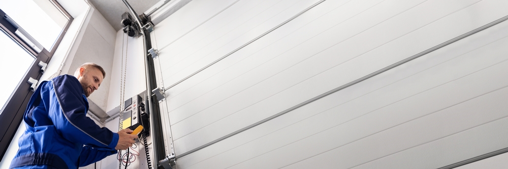 Technician installing and repairing a residential garage door system with tools and hardware components.