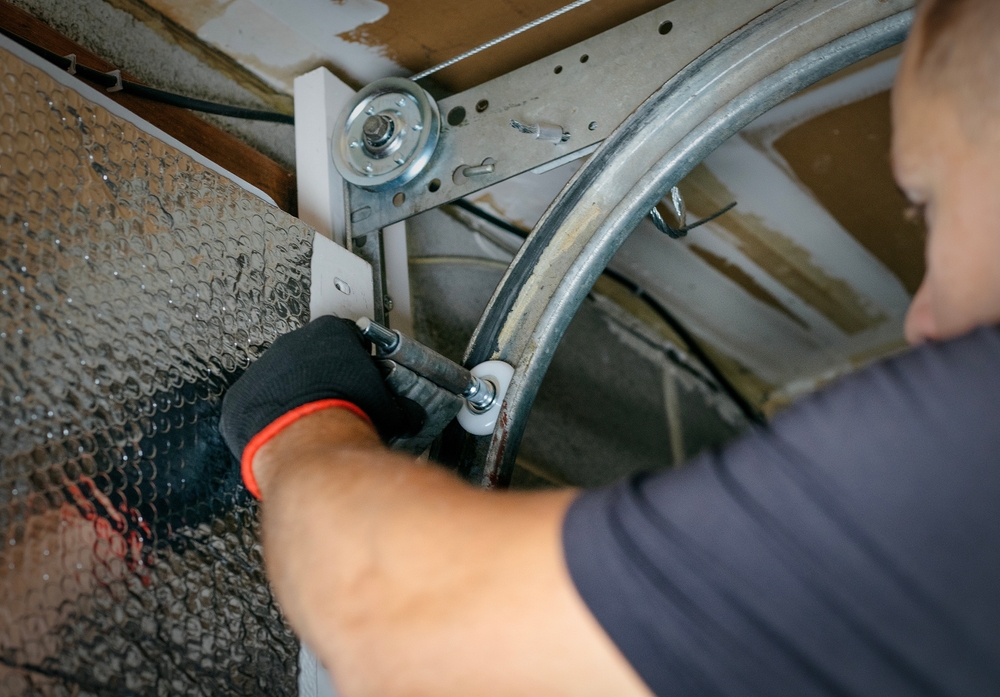 ManRepairingGarageDoorFromInside Technician repairing garage door inside a residential home to fix common issues